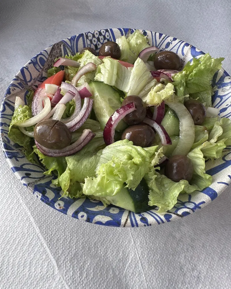 Mixed fresh salad with olives, red onion and cucumber in a blue and white bowl